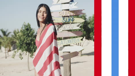 animation of usa flag stripes over happy biracial woman in american flag dancing on sunny beach