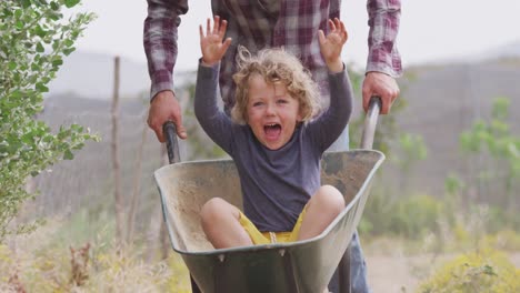 Happy-caucasian-father-and-son-pushing-wheelbarrow