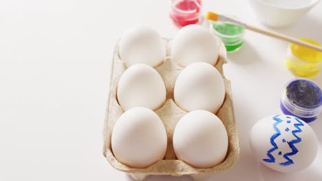 white eggs with colorful paints and brush on white background with copy space