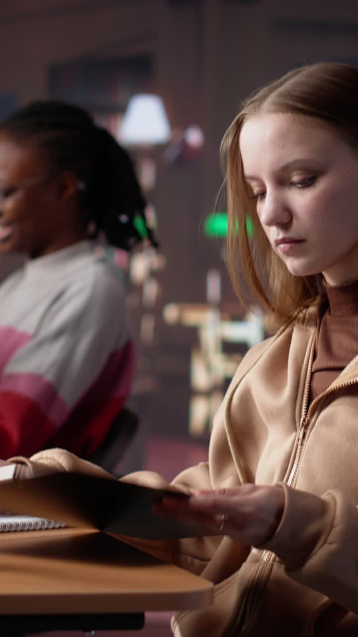 Vertical video young girl listening to educational documentary on laptop and taking notes