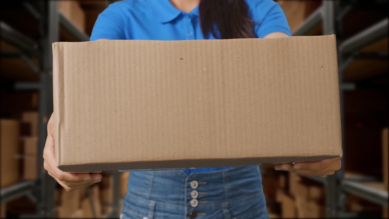 close up de una mensajera femenina en uniforme azul mostrando un cartón a la cámara mientras lo entrega en el almacén