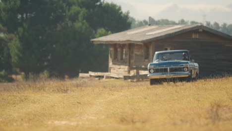 friends driving in pick up truck across field on road trip with cabin in background