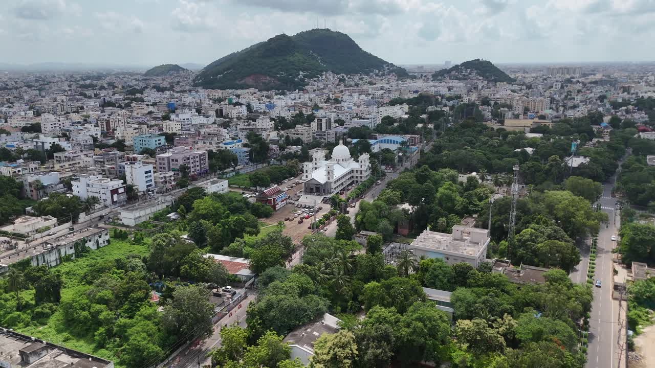 Aerial drone footage of Vijayawada city with the picturesque hill framing the vibrant cityscape below.
