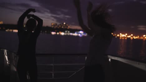 silhouette of two beautiful young women dancing on ship deck at night. girlfriends on the boat