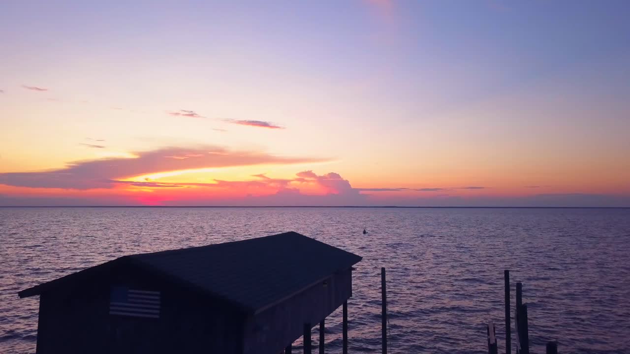 고독한 카약 선수가 형형색색의 일몰 속으로 서서히 흘러가는 극적인 드론 샷