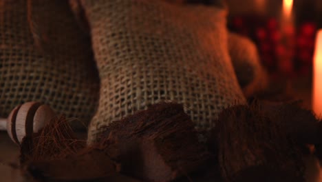 Relaxing-background-close-up-shot-of-some-dry-coconut-pieces,-some-small-bags,-glass-jars,-with-candles-with-flickering-flames-in-the-background-and-some-dust-flying-around