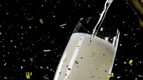 Golden-confetti-falling-over-champagne-pouring-into-a-glass-against-black-background