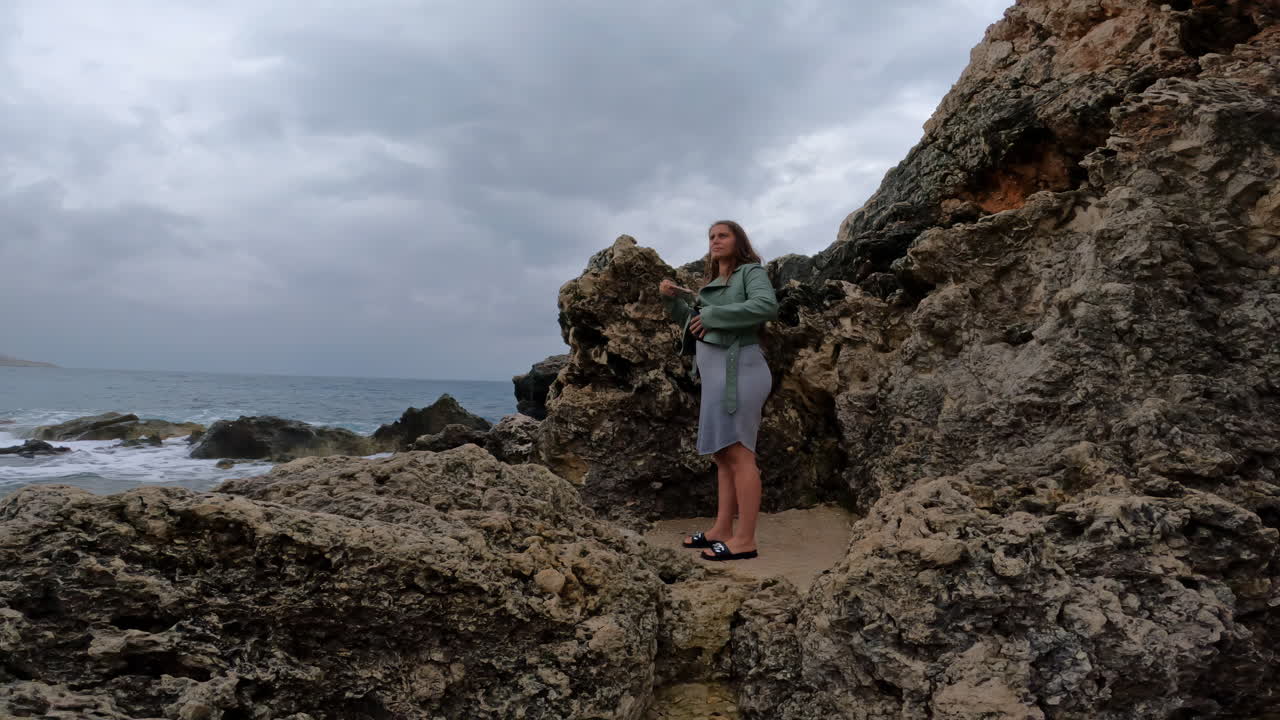 Uma mulher grávida está de pé na costa rochosa da ilha de Malta, no Mediterrâneo.