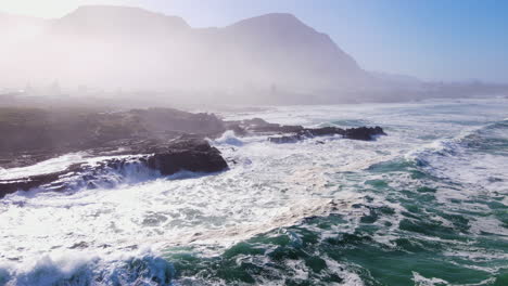 waves pounding rugged shoreline - frothing seawater with misty mountain background