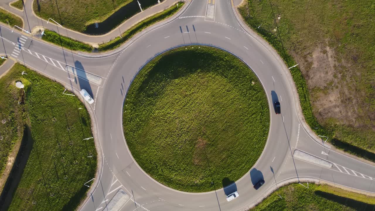 Aerial view of cars driving on roundabout in Katlakalns neighboorhood and residential area in Riga, surrounded by green grass and vegetation, on a sunny spring day in Latvia