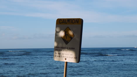 erosion warning sign on waikiki beachfront, ocean waves in background, handheld