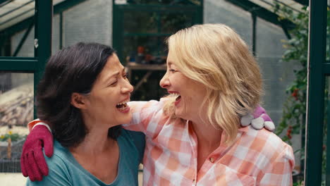 portrait of loving same sex mature female couple hugging as they garden in greenhouse together