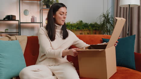 Happy-young-woman-shopper-unpacking-cardboard-box-delivery-parcel-online-shopping-purchase-at-home