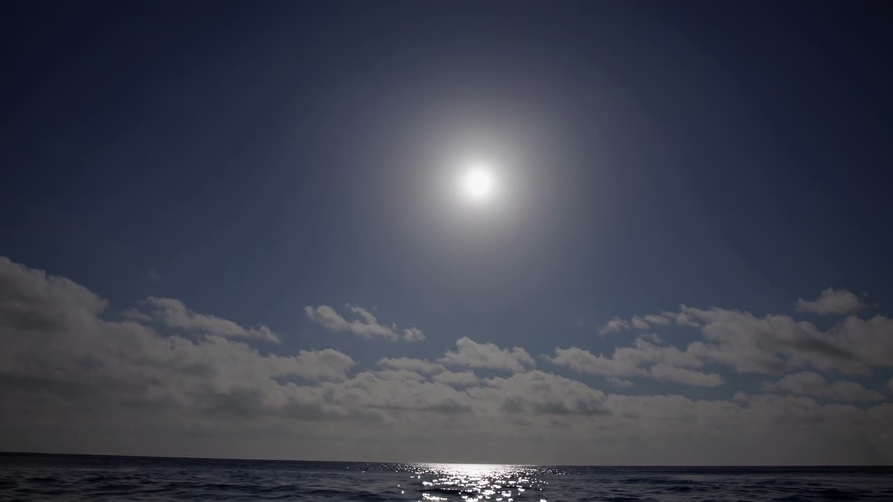 Uma vista serena do oceano sob um sol forte, capturada de uma perspectiva de ângulo baixo, criando uma sensação de calma