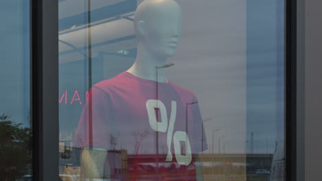 mannequin with red percentage discount t-shirt in clothing store shopwindow, handheld footage