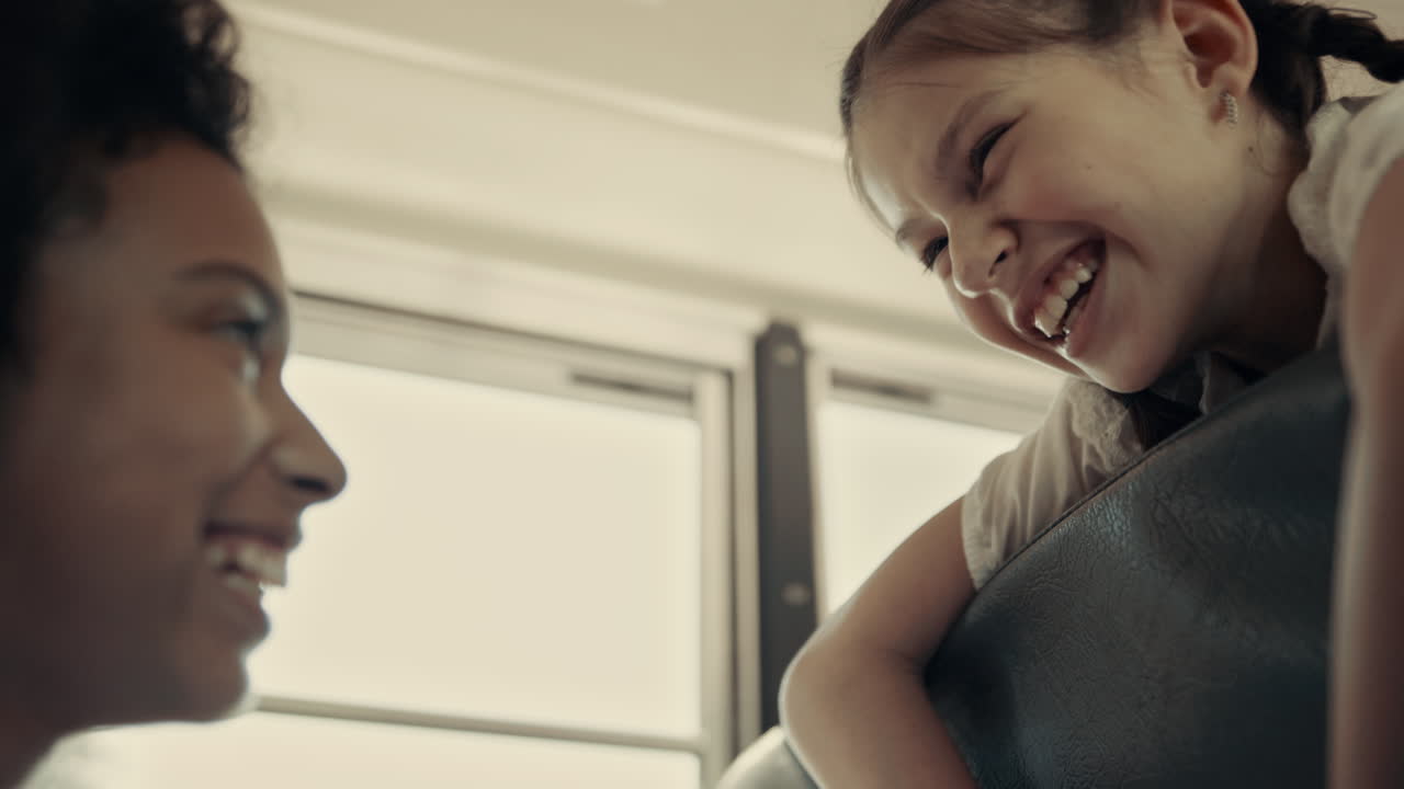 Two schoolgirls laughing sitting school bus close up. Teens chatting in vehicle