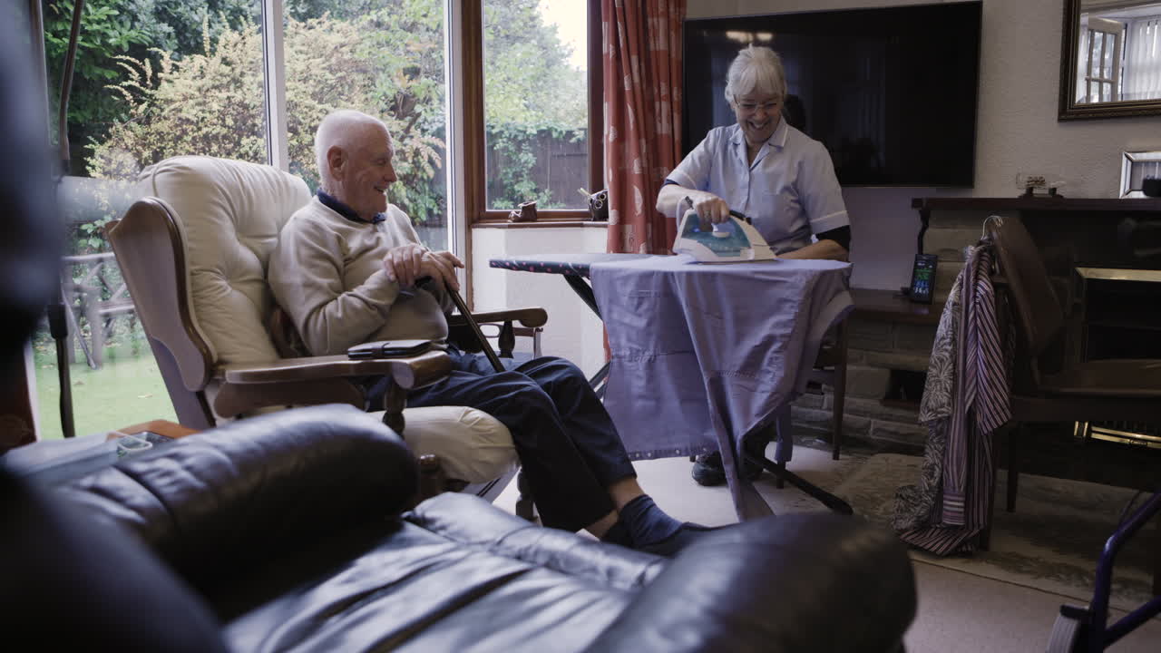 Elderly man relaxing while caregiver irons in living room