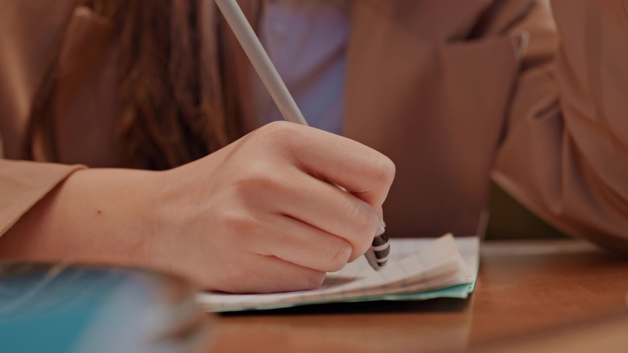 Hand writing in notebook at wooden table, pen nib gliding across paper, entrepreneur drafting plan and notes, contracts and agenda nearby, steady wrist, focused detail, productivity mood