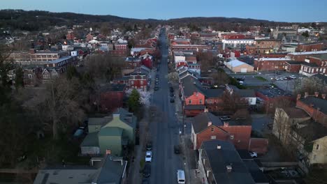 Aerial-descending-shot-of-main-road-in-american-city-during-dusk---residential-area-with-different-colonial-houses-near-park