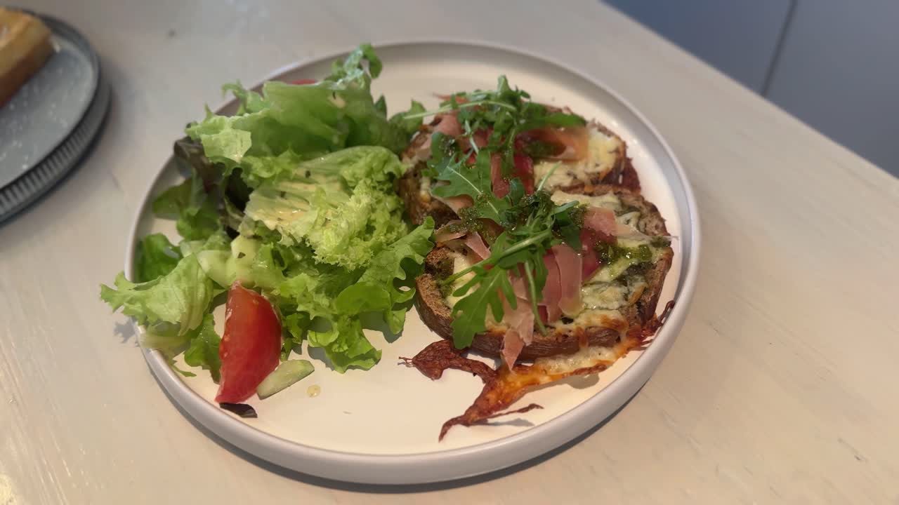 Close-up shot of a healthy mixed salad with greens, tomatoes, and toast on a white plate in a cozy restaurant