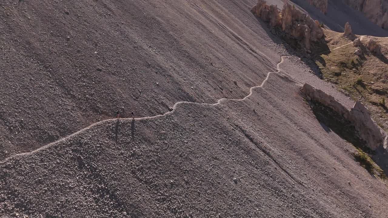 Drone rotating while filming two persons walking on a mountainous path in 4k