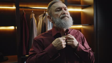 morning routine. close up portrait of stylish mature bearded man putting on shirt, getting ready for work at wardrobe