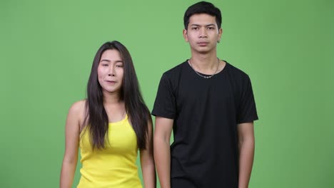 young asian couple pointing at camera together