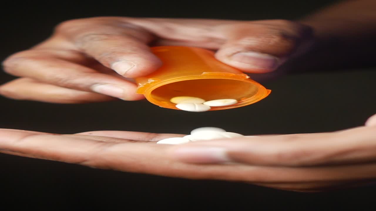la mano de una persona sosteniendo un frasco de pastillas y dispensando pastillas