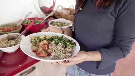 vista de las manos de una niña mientras sirve comida saludable y natural para el almuerzo tomándola de tazones de colores colocados sobre una mesa