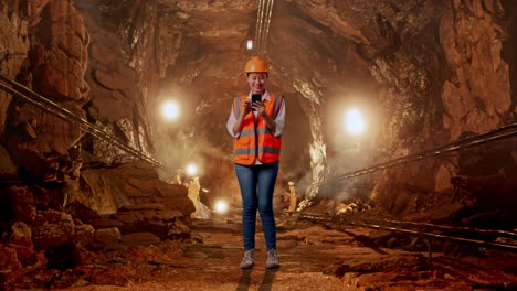 full body of asian female engineer with safety helmet using smartphone in underground mine tunnel