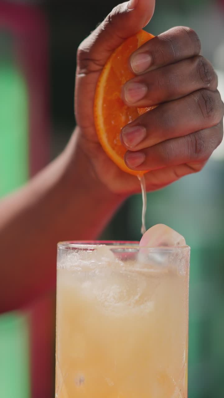 el camarero exprime la mitad de la naranja en un cóctel en un bar de primer plano. el camarero afroamericano agrega un ingrediente de cítricos frescos para beber en un club nocturno. bebida de fiesta