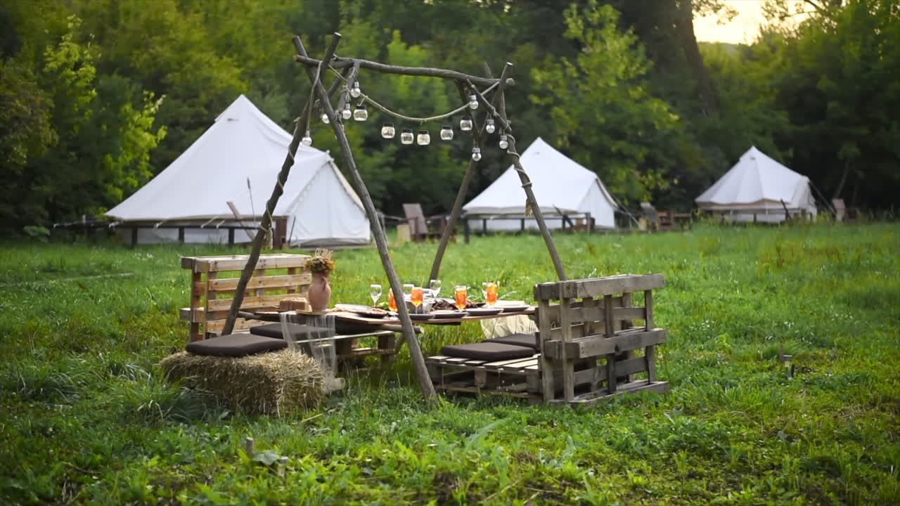 Tavolo con cibo e bevande al glamping, vegetazione circostante, tende sullo sfondo
