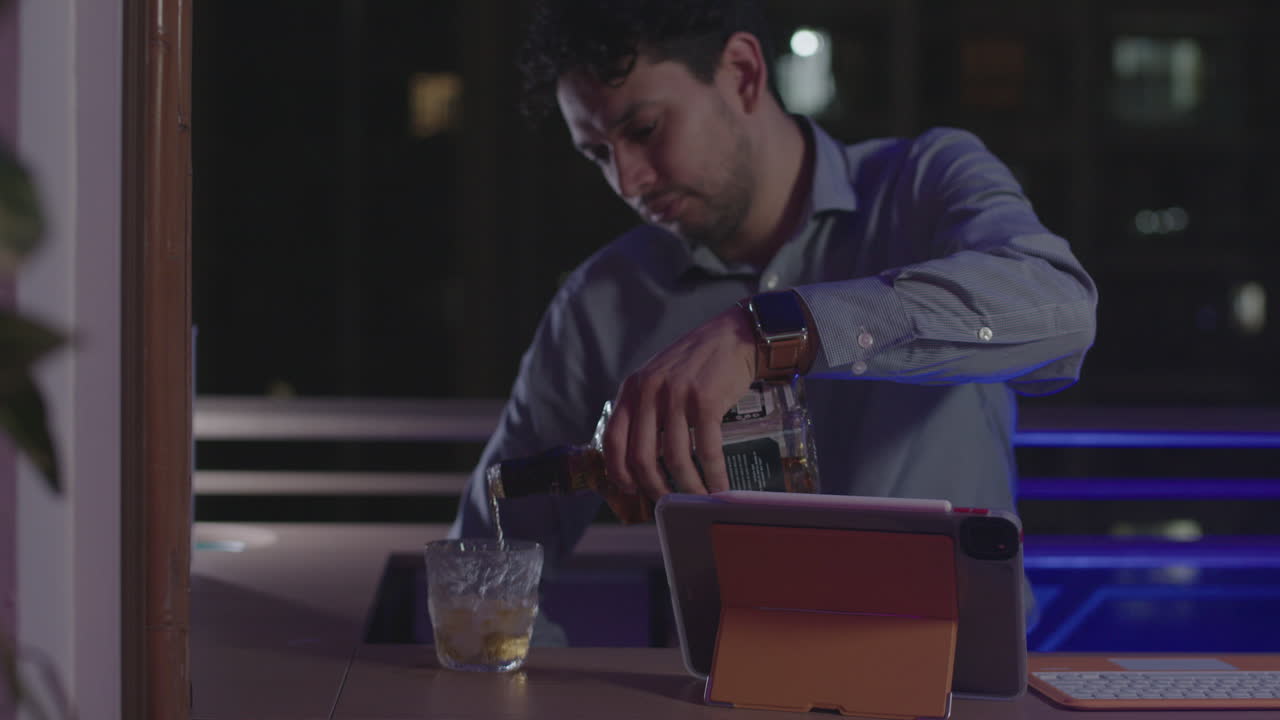 Primo piano di una mano maschile che tiene una bottiglia di bevanda alcolica e riempie un bicchiere di whisky.