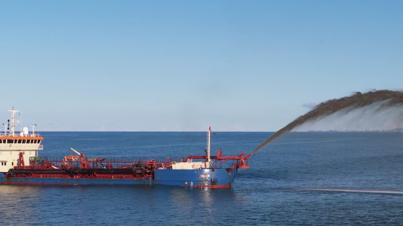 Una grande draga blu spruzza una miscela di sabbia e acqua nel mare