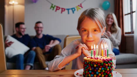 a young girl celebrates her birthday with a cake and lit candles, surrounded by family at home