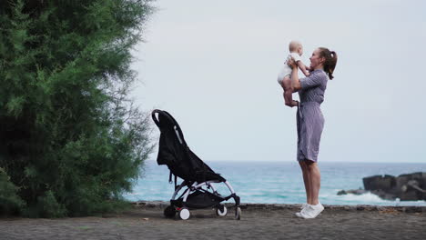 On-the-seashore,-the-mother-joyfully-throws-her-son-into-the-air-and-engages-in-playful-interaction.-A-young,-cheerful-family-enjoys-the-beach