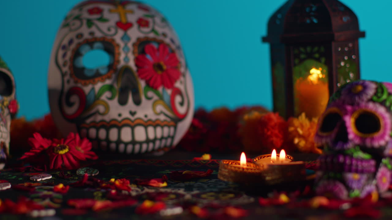 primer plano de cráneos y máscaras decoradas rodeadas de velas y pétalos de flores celebrando la fiesta mexicana de dia de muertos o día de los muertos contra un fondo azul 3