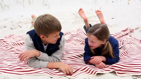 Siblings-lying-on-blanket-on-the-beach-talking