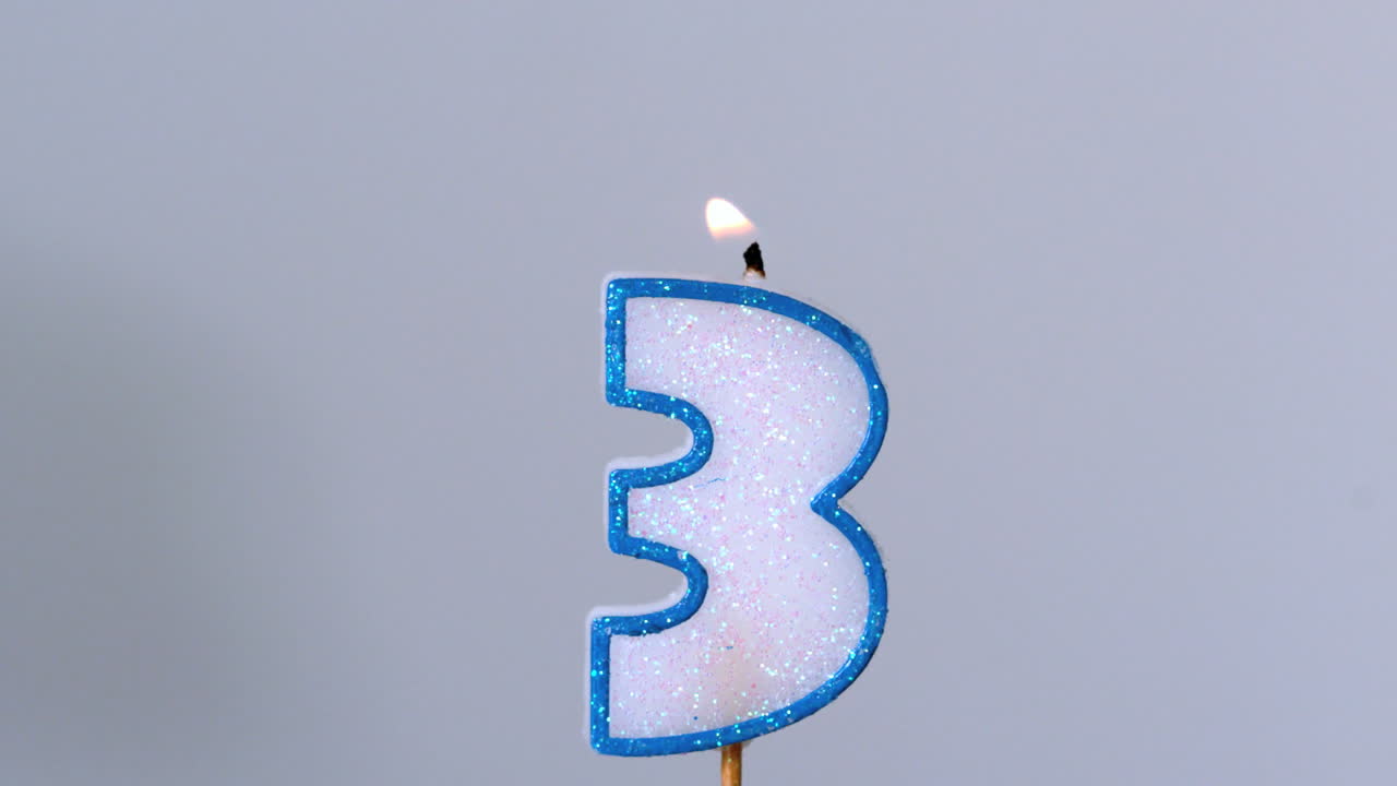 tres velas de cumpleaños parpadeando y apagándose sobre un fondo azul