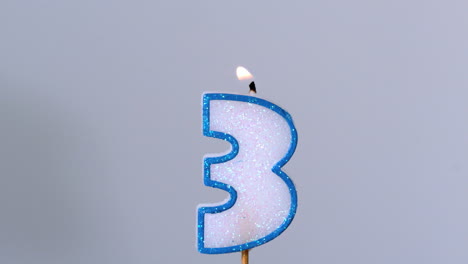 Three-birthday-candle-flickering-and-extinguishing-on-blue-background