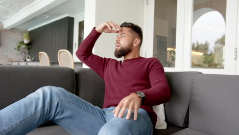 sitting on couch, man annoyed looking at message on phone in modern living room
