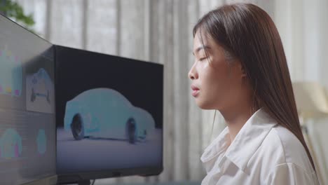 아시아 여성 자동차 디자이너가 스튜디오의 데스크 컴퓨터에서 ev 자동차의 3d 모델을 작업하는 동안 스트레칭하는 가까운 측면 뷰