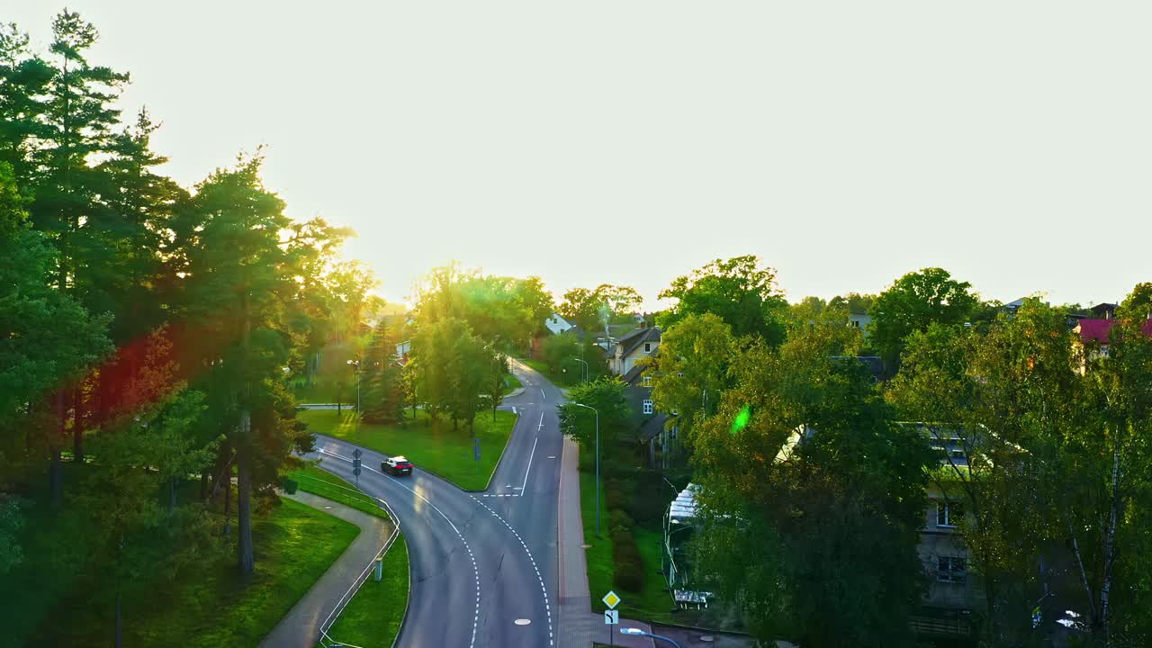 Serene road curving through forested town with sunset light and car passing
