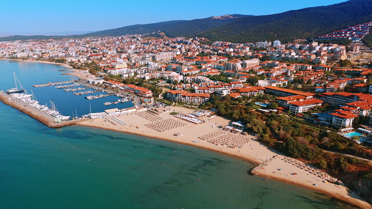 Yacht club with multiple boats and sandy beach with numerous seats for the vacationers at the shore of the Black Sea. Lots of hotels locate on the green slope of the mountains in Sveti Vlas, Bulgaria