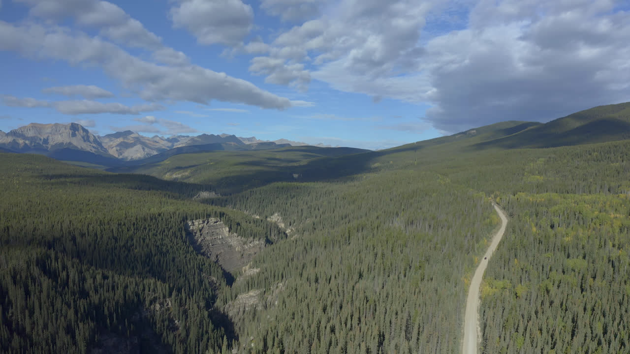 Ampia vista di una foresta di conifere con strada di campagna e montagne rocciose vicino a Nordegg, Alberta, Canada.