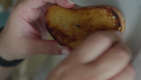 video vertical que muestra una mano frotando una rebanada de pan tostado de color marrón dorado con un diente de ajo asado