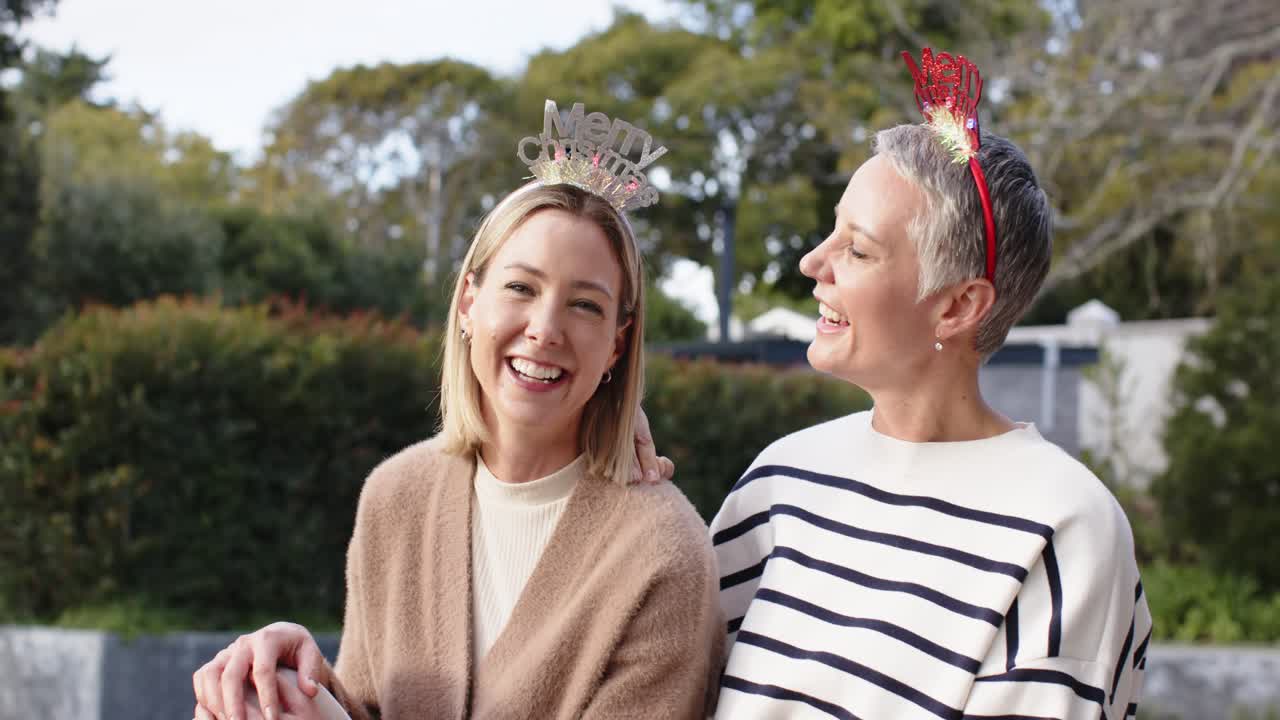 Mamma och dotter sitter på trädgårdsmuren med Merry Christmas-diadem och sprider julstämning