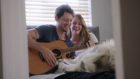 couple playing guitar with dog in bed