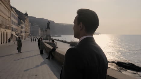 man in a suit looking at the sea from a coastal promenade at sunset