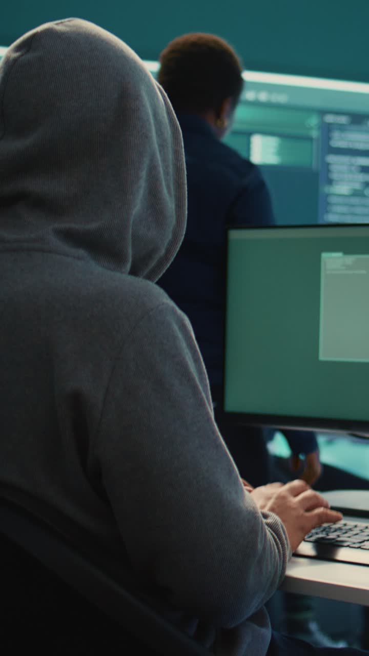 Hætteklædt hacker, der skriver på computer i et mørkt serverrum